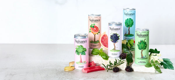 Collection of Nuisance Drinks cans supplement cans on a white surface with various herbs and fruits.